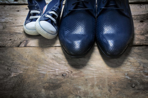 father's business shoes and kids sneakers side by side on rustic wood, concept of family, single parent and father's day, view from above